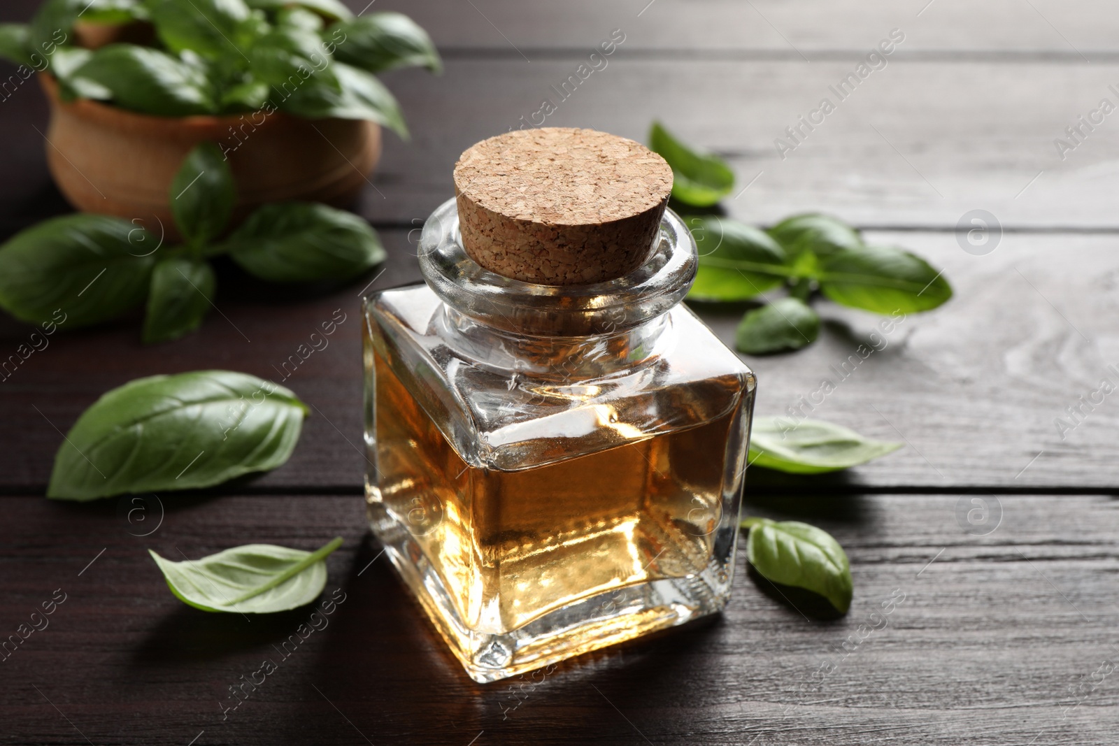 Photo of Bottle of basil essential oil and green leaves on wooden table