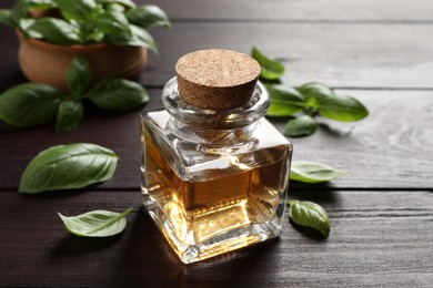 Photo of Bottle of basil essential oil and green leaves on wooden table