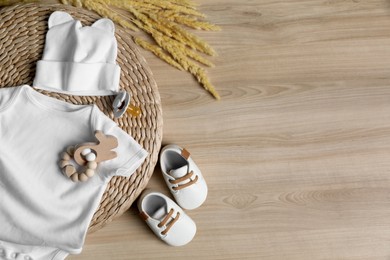 Baby bodysuit, hat, booties, toy and spikelets on wooden background, flat lay. Space for text