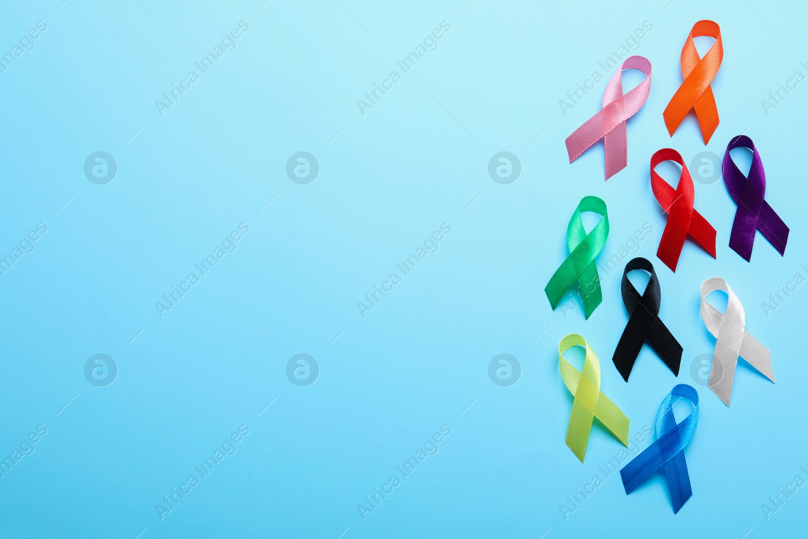 Photo of Colorful ribbons on light blue background, flat lay with space for text. World Cancer Day