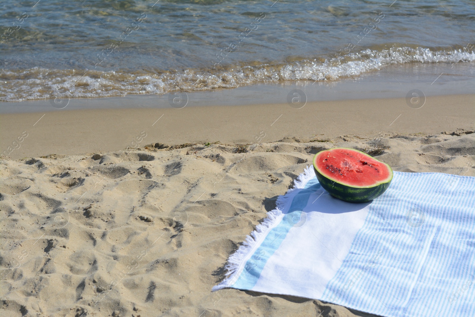 Photo of Half of fresh juicy watermelon on beach blanket near sea, space for text