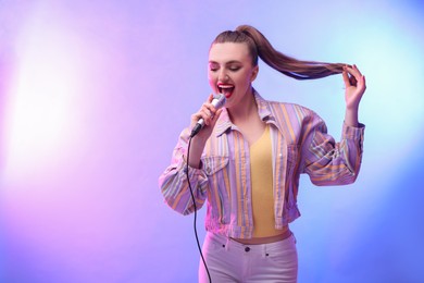 Photo of Emotional woman with microphone singing in color lights. Space for text