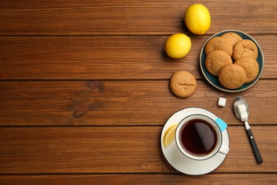 Photo of Flat lay composition with tea bag in ceramic cup of hot water, cookies and lemon on wooden table. Space for text