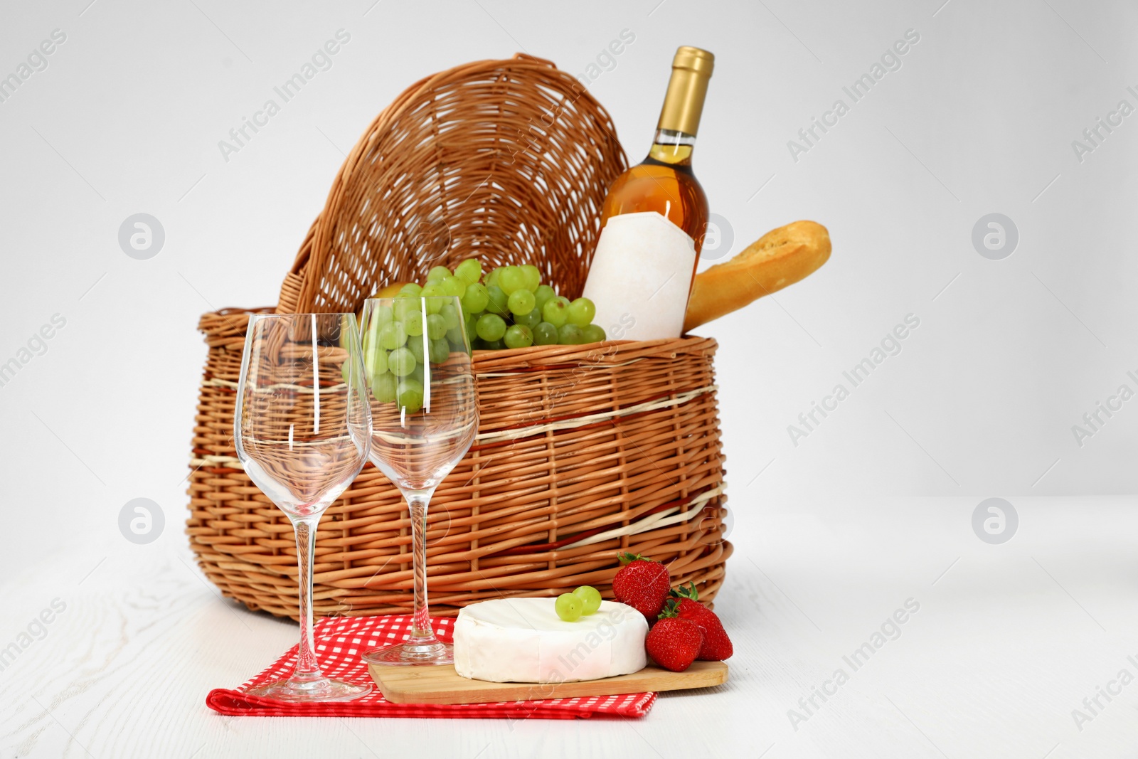 Photo of Picnic basket with wine, glasses and products on white background