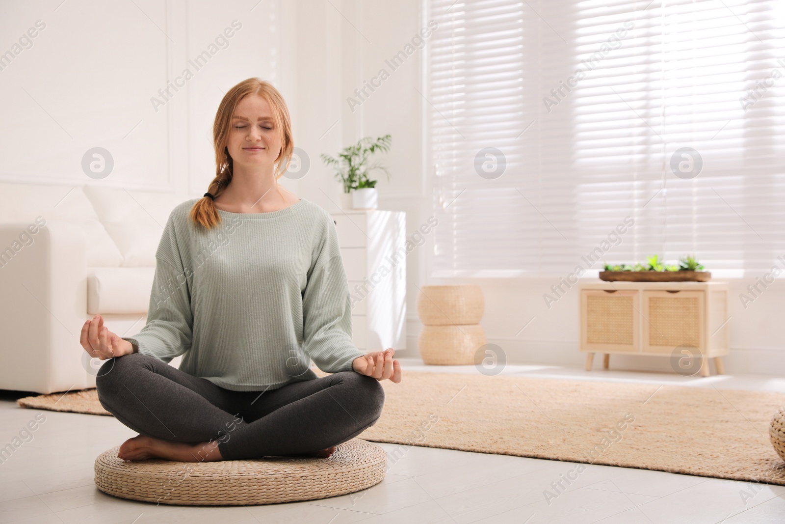 Photo of Woman meditating on wicker mat at home. Space for text