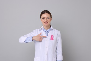 Photo of Mammologist pointing at pink ribbon against grey background. Breast cancer awareness