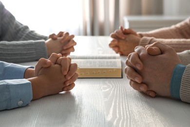 Photo of Boy and his godparents praying together at white wooden table indoors, closeup