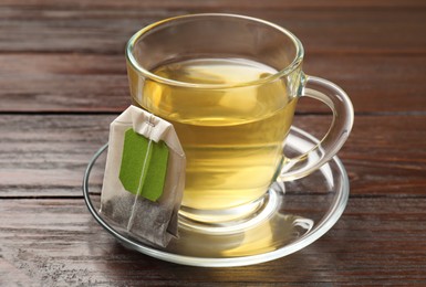 Photo of Tea bag and glass cup of hot beverage on wooden table, closeup
