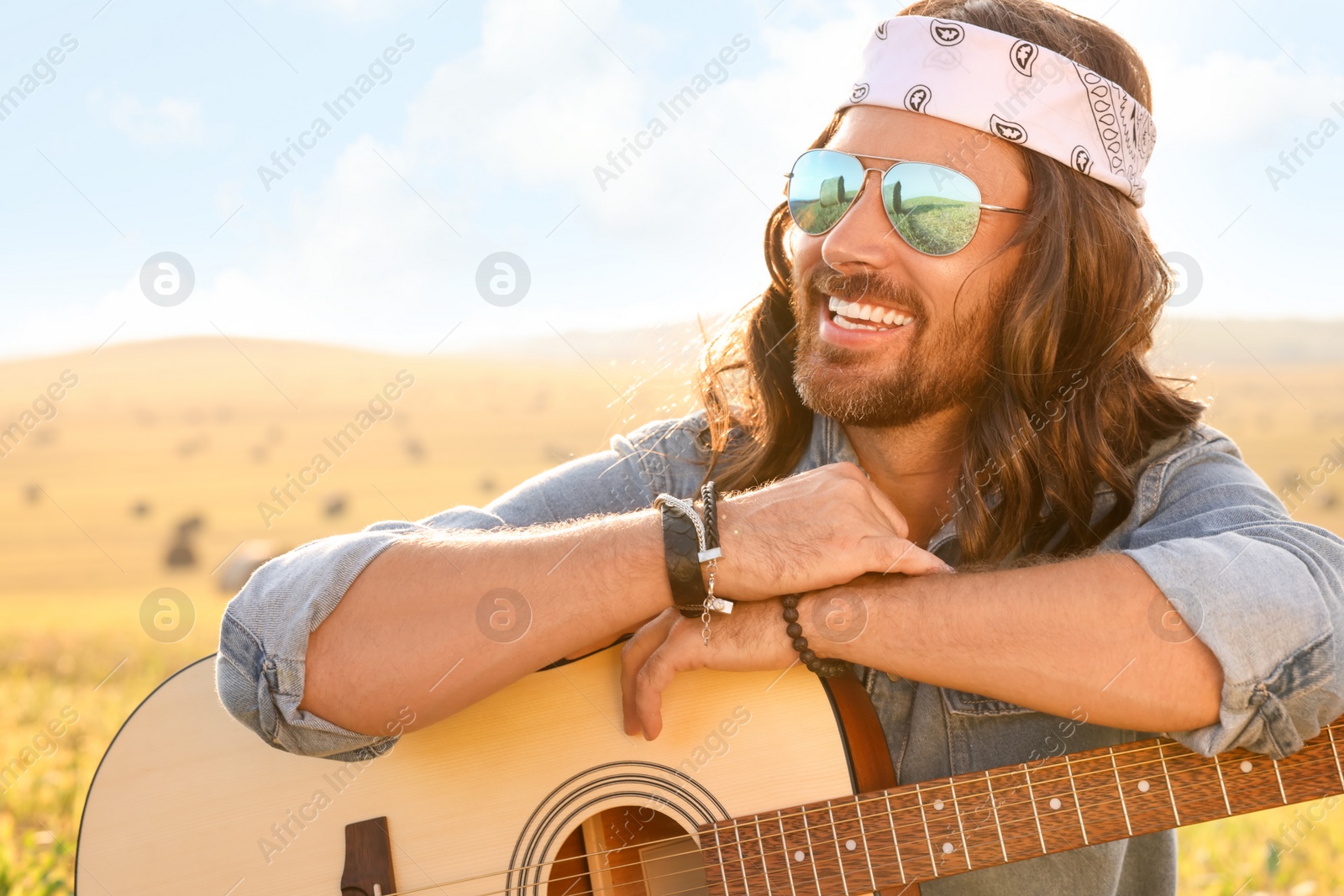 Photo of Portrait of happy hippie man with guitar in field