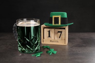 Photo of St. Patrick's day celebrating on March 17. Green beer, wooden block calendar, leprechaun hat and decorative clover leaves on grey table