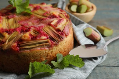 Photo of Freshly baked rhubarb pie, green leaves and cake server on wooden table, closeup
