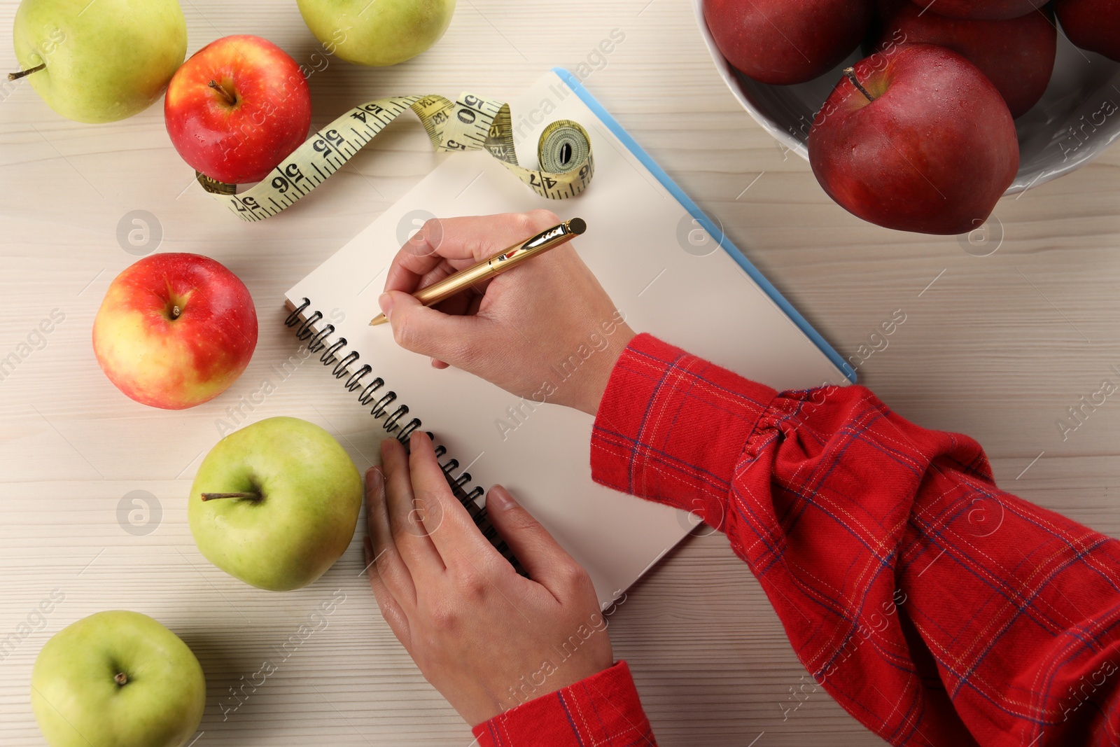 Photo of Woman developing diet plan at light wooden table with apples and measuring tape, top view