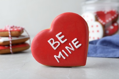Delicious heart shaped cookie with phrase Be Mine on light table, closeup. Valentine's Day