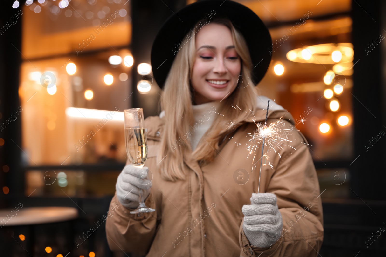 Photo of Happy young woman with sparkler and glass of champagne at winter fair