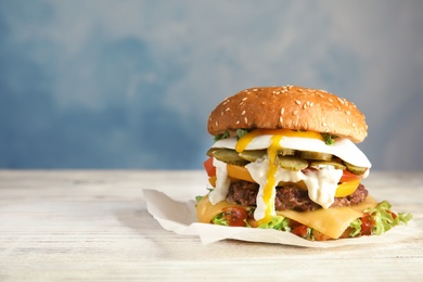 Tasty burger with fried egg on parchment against color background, space for text