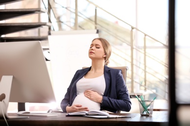 Photo of Young pregnant woman suffering from pain while working in office