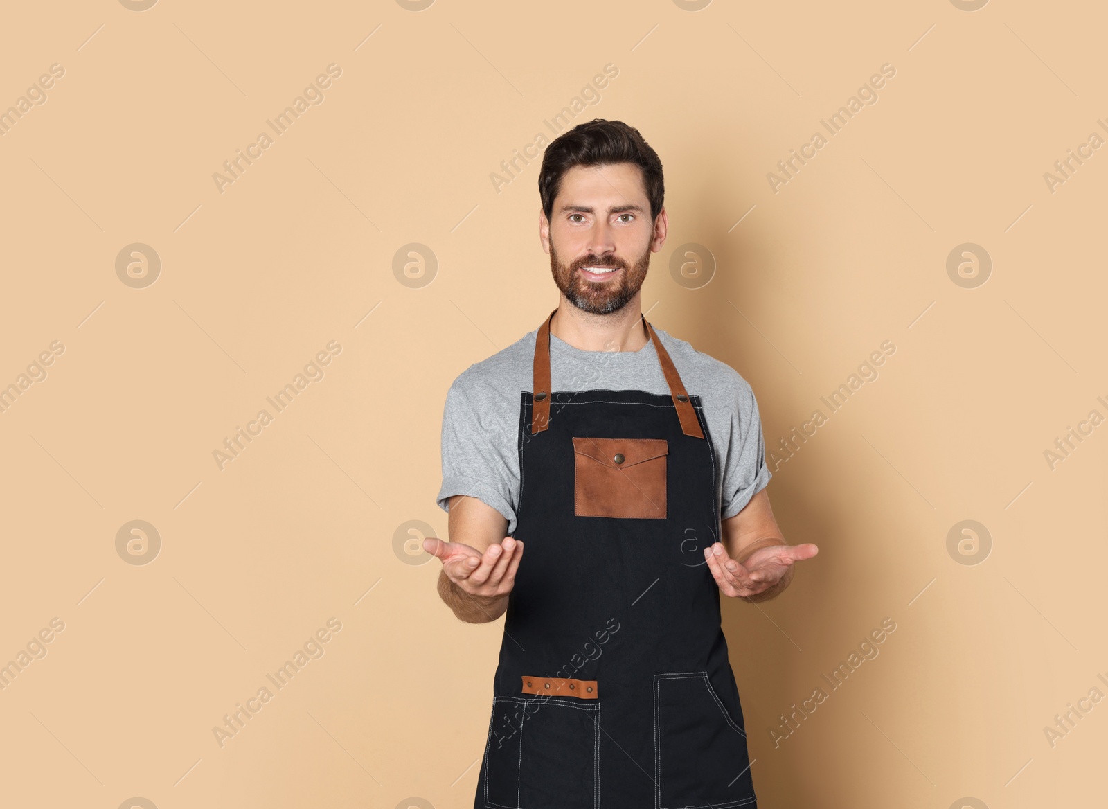 Photo of Smiling hairdresser wearing apron on light brown background, space for text