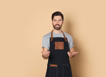 Smiling hairdresser wearing apron on light brown background, space for text