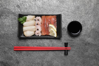 Photo of Sashimi set served with soy sauce, lemon and parsley on light grey table, flat lay