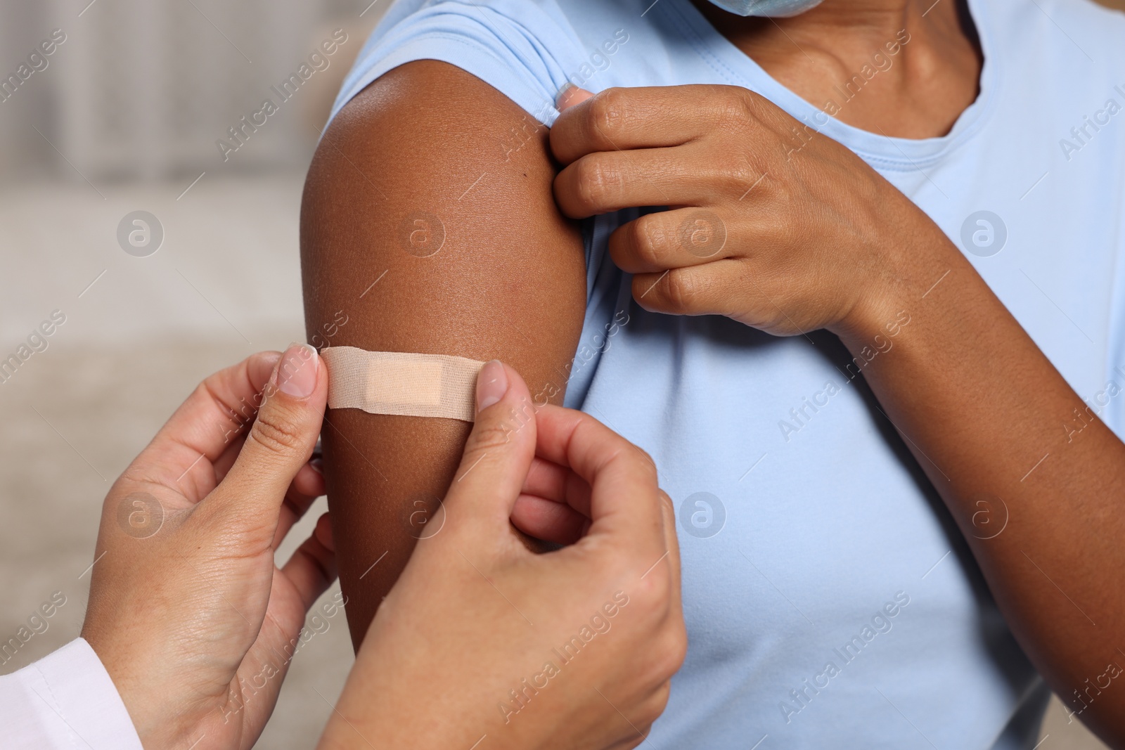 Photo of Doctor putting adhesive bandage on young woman's arm after vaccination indoors, closeup