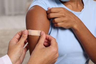 Doctor putting adhesive bandage on young woman's arm after vaccination indoors, closeup