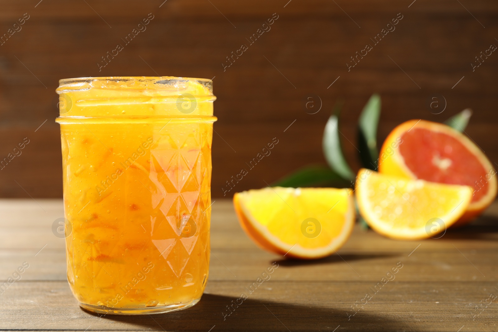 Photo of Delicious orange marmalade and fresh fruits on wooden table. Space for text