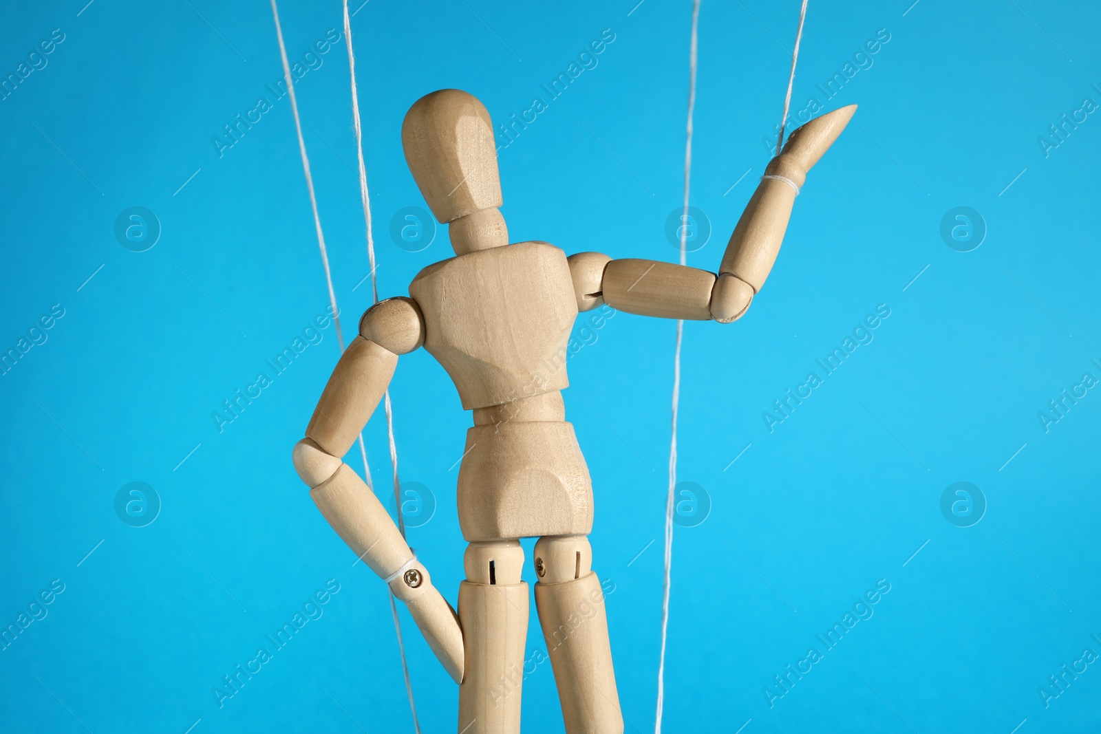 Photo of One wooden puppet with strings on light blue background