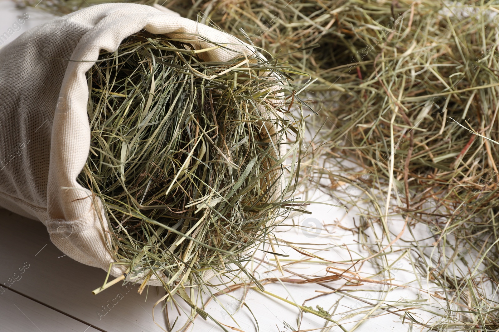 Photo of Burlap sack with dried hay on white wooden table, closeup