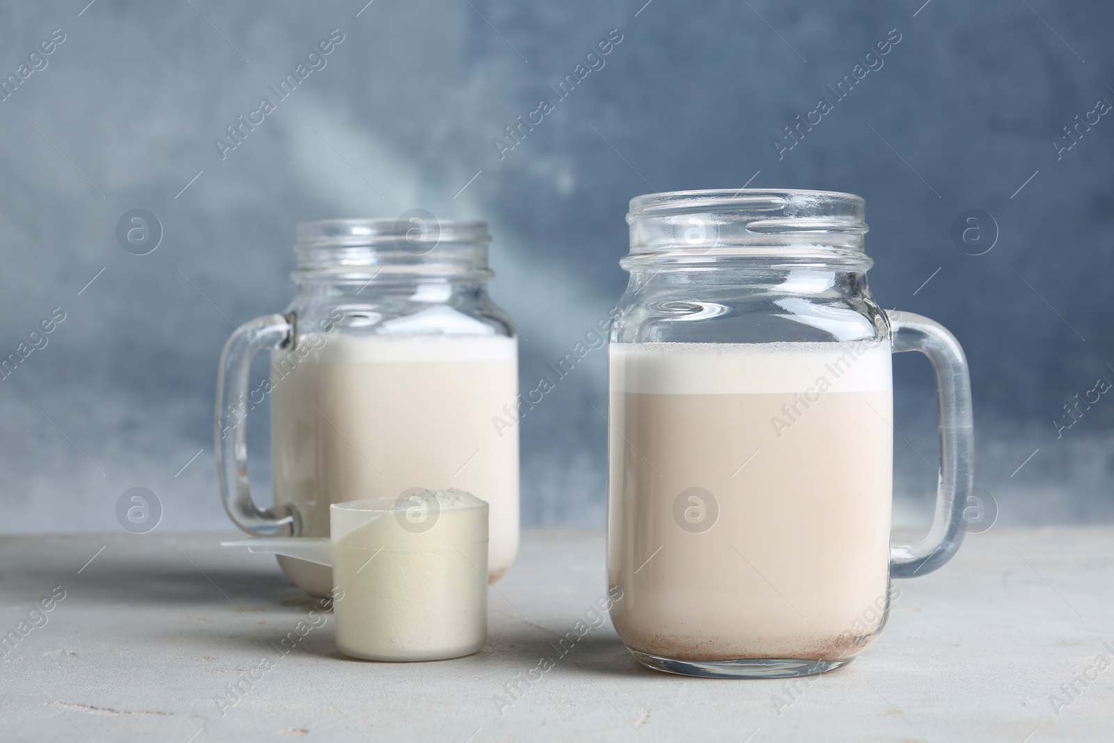 Photo of Mason jars with protein shake and scoop of powder on table