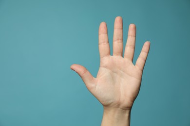 Left-handed woman holding open palm on light blue background, closeup. Space for text