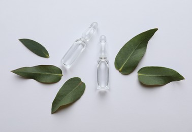 Photo of Pharmaceutical ampoules and green leaves on white background, flat lay