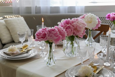 Stylish table setting with beautiful peonies and burning candles indoors