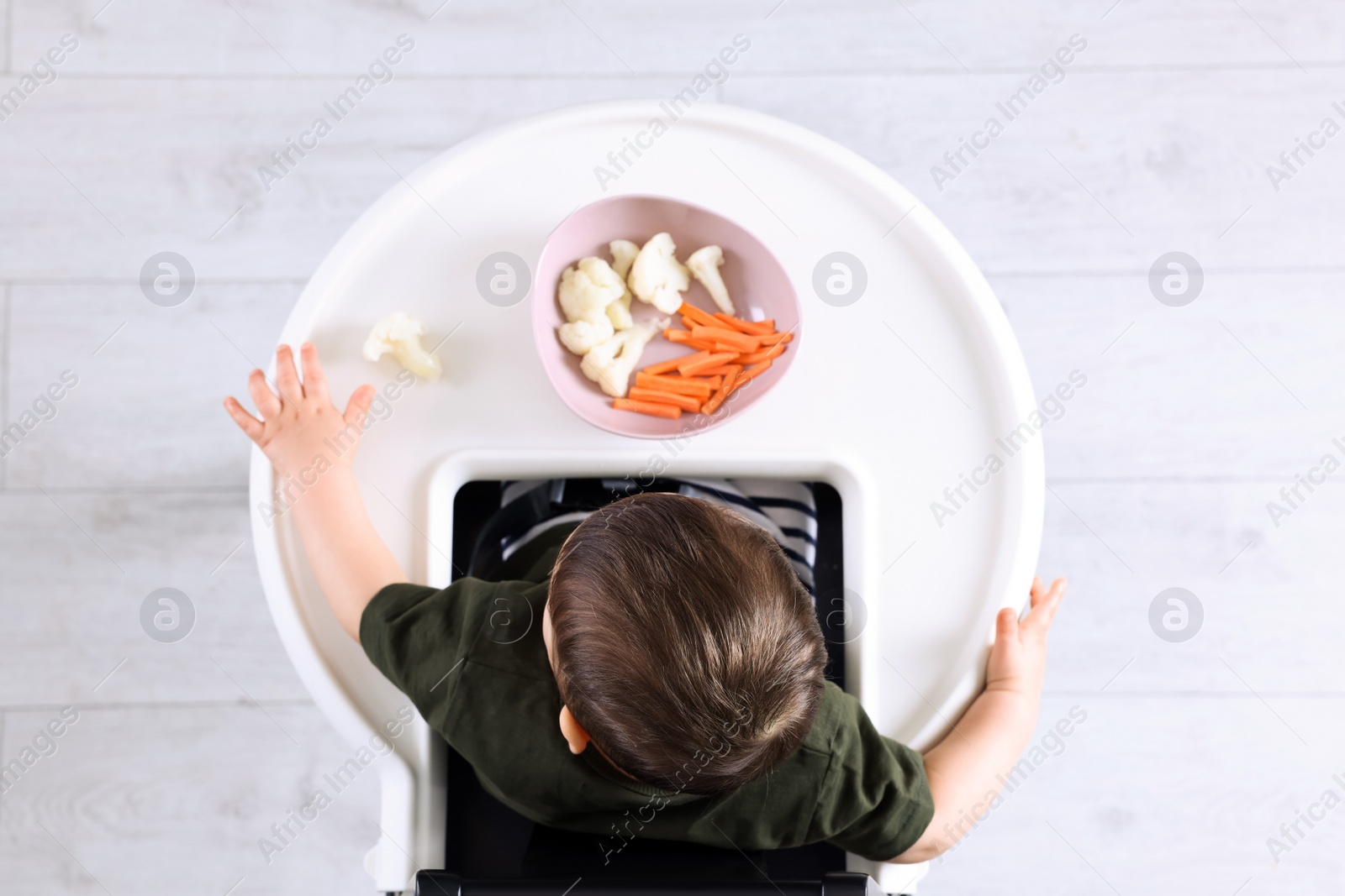 Photo of Cute little baby eating healthy food in high chair indoors, top view