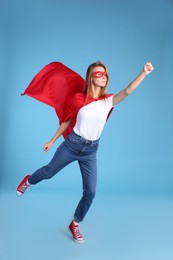 Photo of Confident woman wearing superhero cape and mask on light blue background