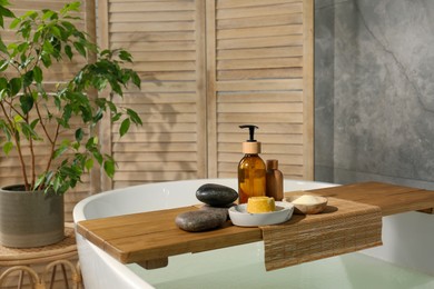 Photo of Wooden tray with spa products and stones on bath tub in bathroom