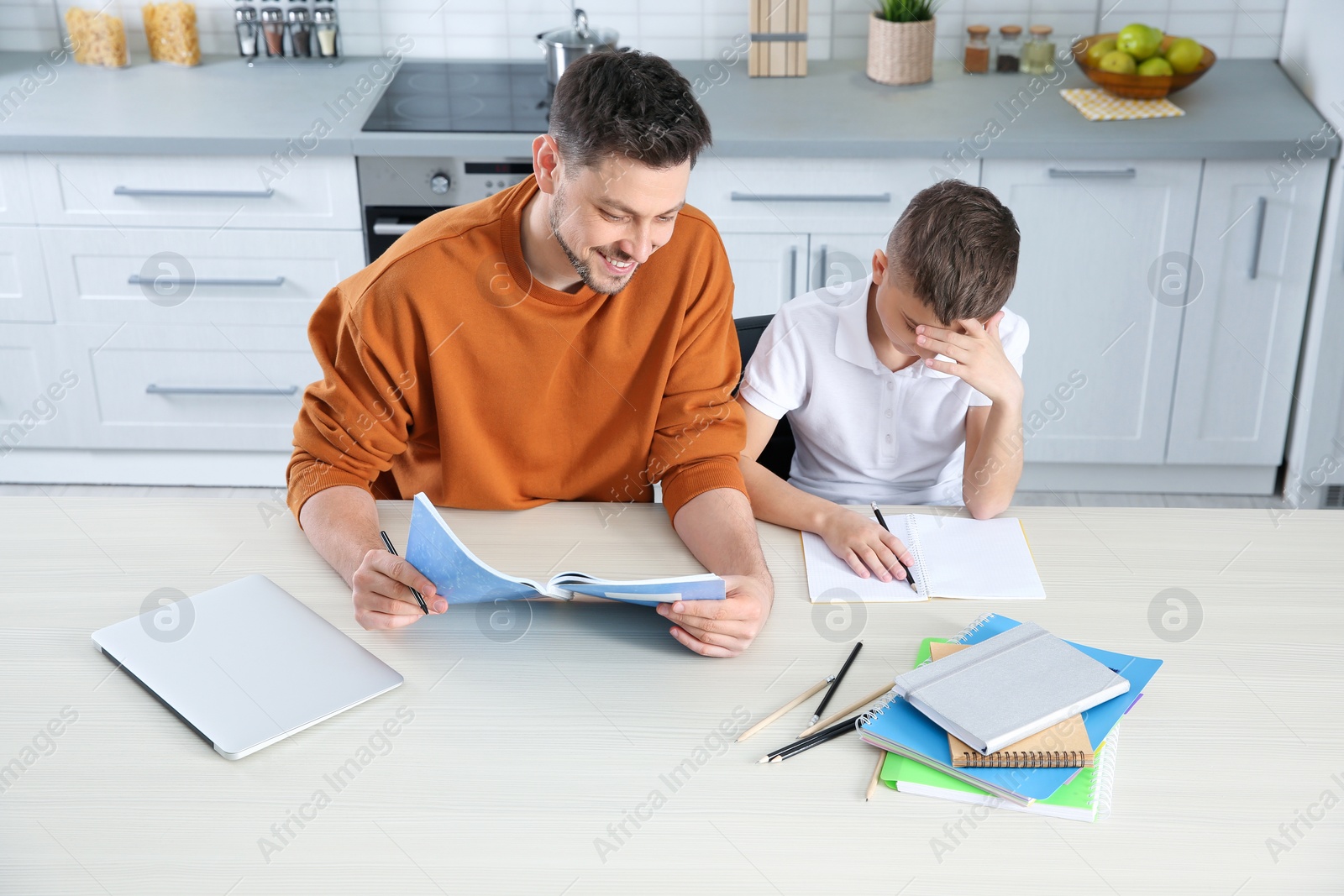 Photo of Dad helping his son with homework in kitchen, above view