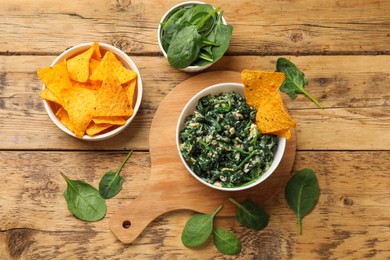 Photo of Tasty spinach dip with eggs in bowl and nachos chips on wooden table, flat lay