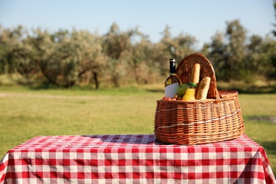 Wicker picnic basket with wine and snacks on table in park. Space for text