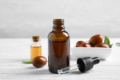 Photo of Glass bottle with jojoba oil and dropper on white wooden table