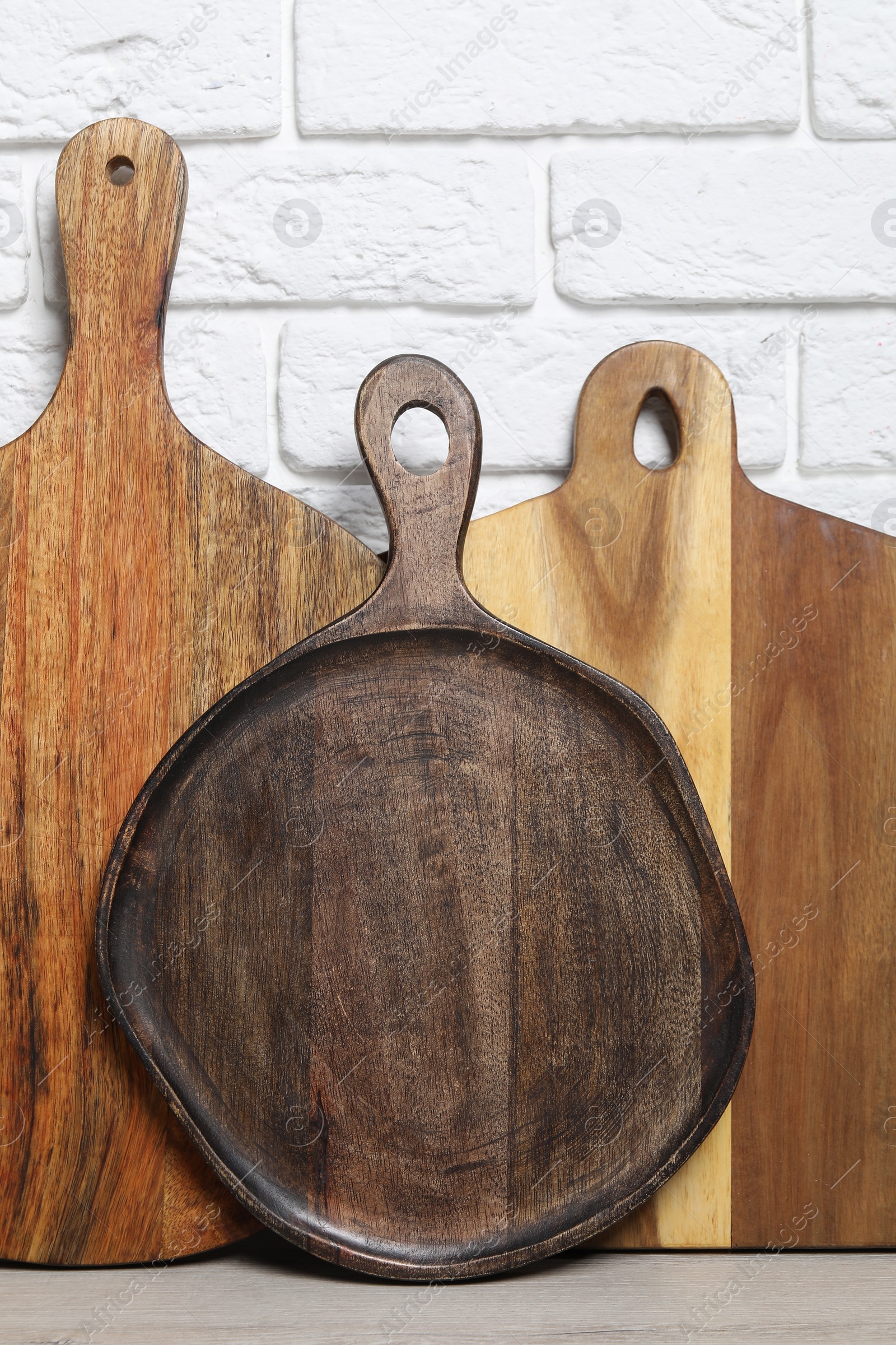 Photo of Different wooden cutting boards on light table near white brick wall