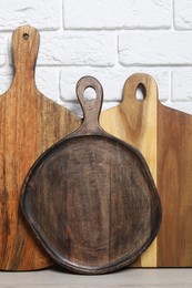 Different wooden cutting boards on light table near white brick wall