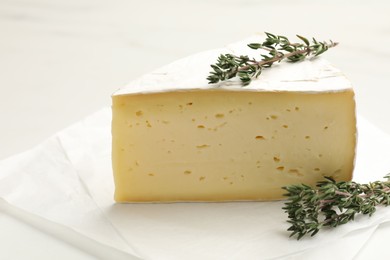 Photo of Piece of tasty camembert cheese and thyme on white table, closeup