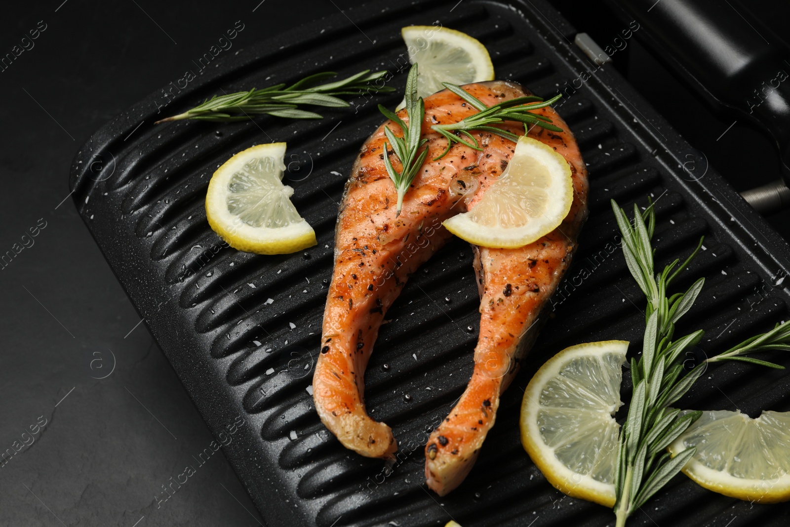 Photo of Cooking salmon. Grill with tasty fish steak, lemon and rosemary on grey table