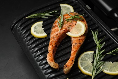 Photo of Cooking salmon. Grill with tasty fish steak, lemon and rosemary on grey table