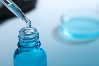 Photo of Dripping liquid from pipette into glass bottle on blurred background, closeup. Space for text