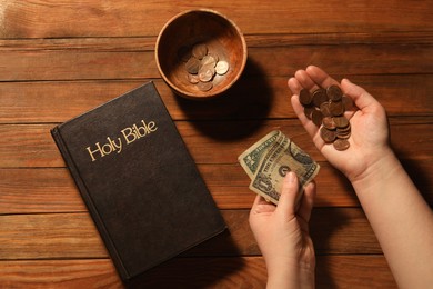 Photo of Donate and give concept. Woman with money, closeup. Bible and bowl of coins on wooden table, top view