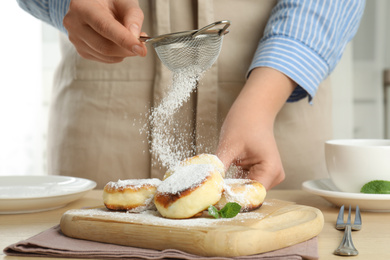 Woman sieving sugar powder on cottage cheese pancakes at wooden table, closeup