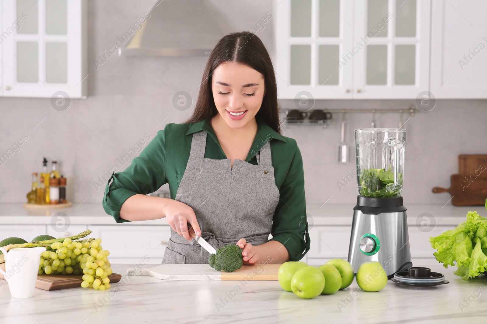 Photo of Young woman cutting broccoli for smoothie at white table in kitchen