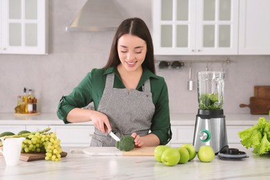 Photo of Young woman cutting broccoli for smoothie at white table in kitchen