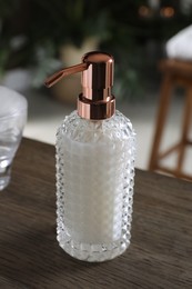 Dispenser of liquid soap on wooden table in bathroom